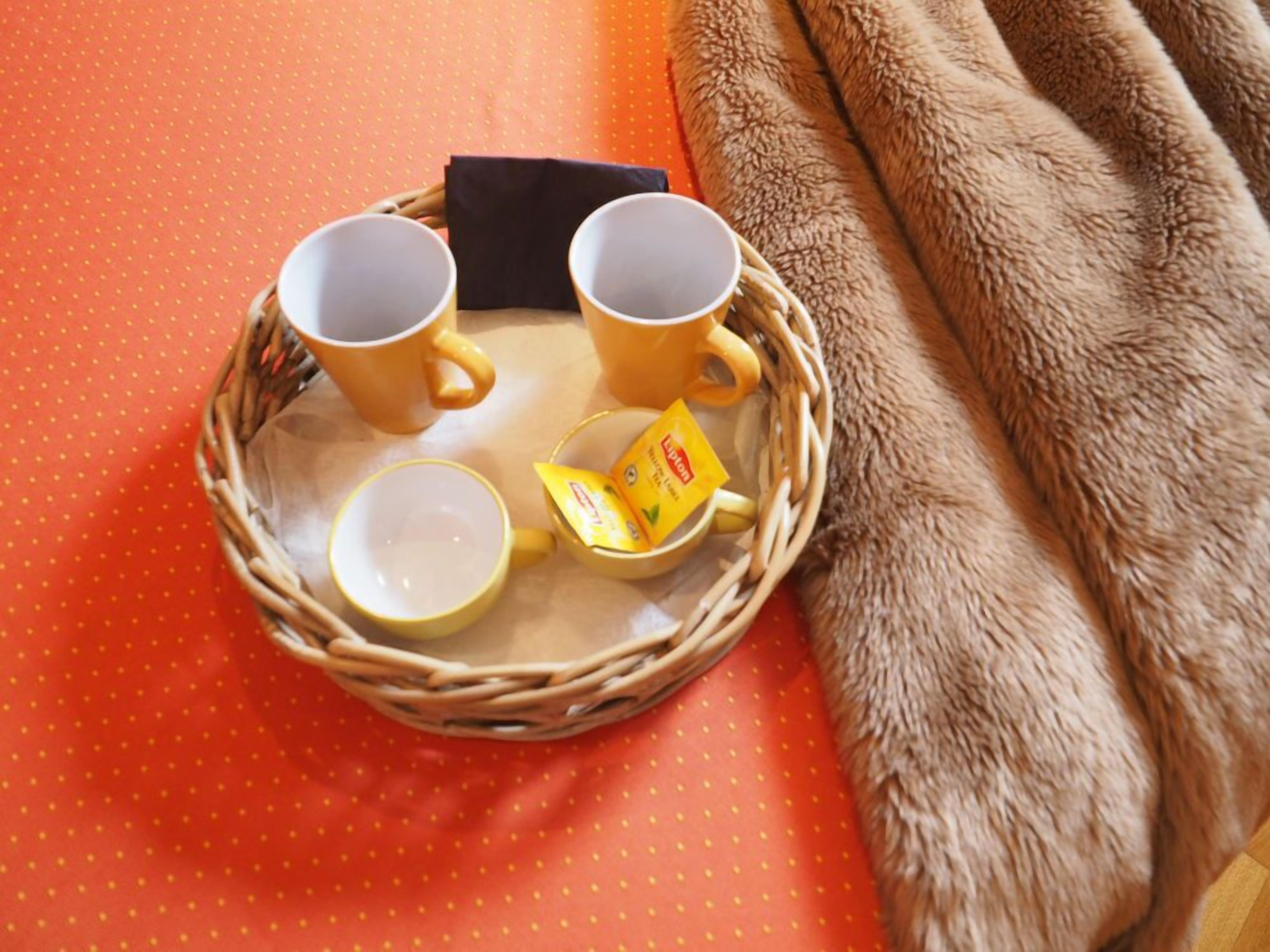 Un plateau en osier avec deux tasses jaunes et une boîte de thé, le tout posé sur une surface orange.