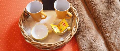 Un plateau en osier avec deux tasses jaunes et une boîte de thé, le tout posé sur une surface orange.
