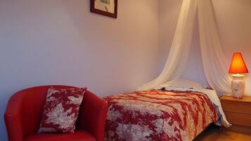 Um quarto com uma cama, uma cadeira vermelha, uma mesa de cabeceira com abajur e um dossel translúcido sobre a cama.
