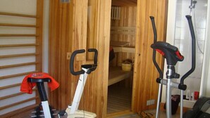 A small room with a wooden sauna, a treadmill, and a stationary bike. - Chambres d'hôtes La Bruyère (May-sur-Orne)