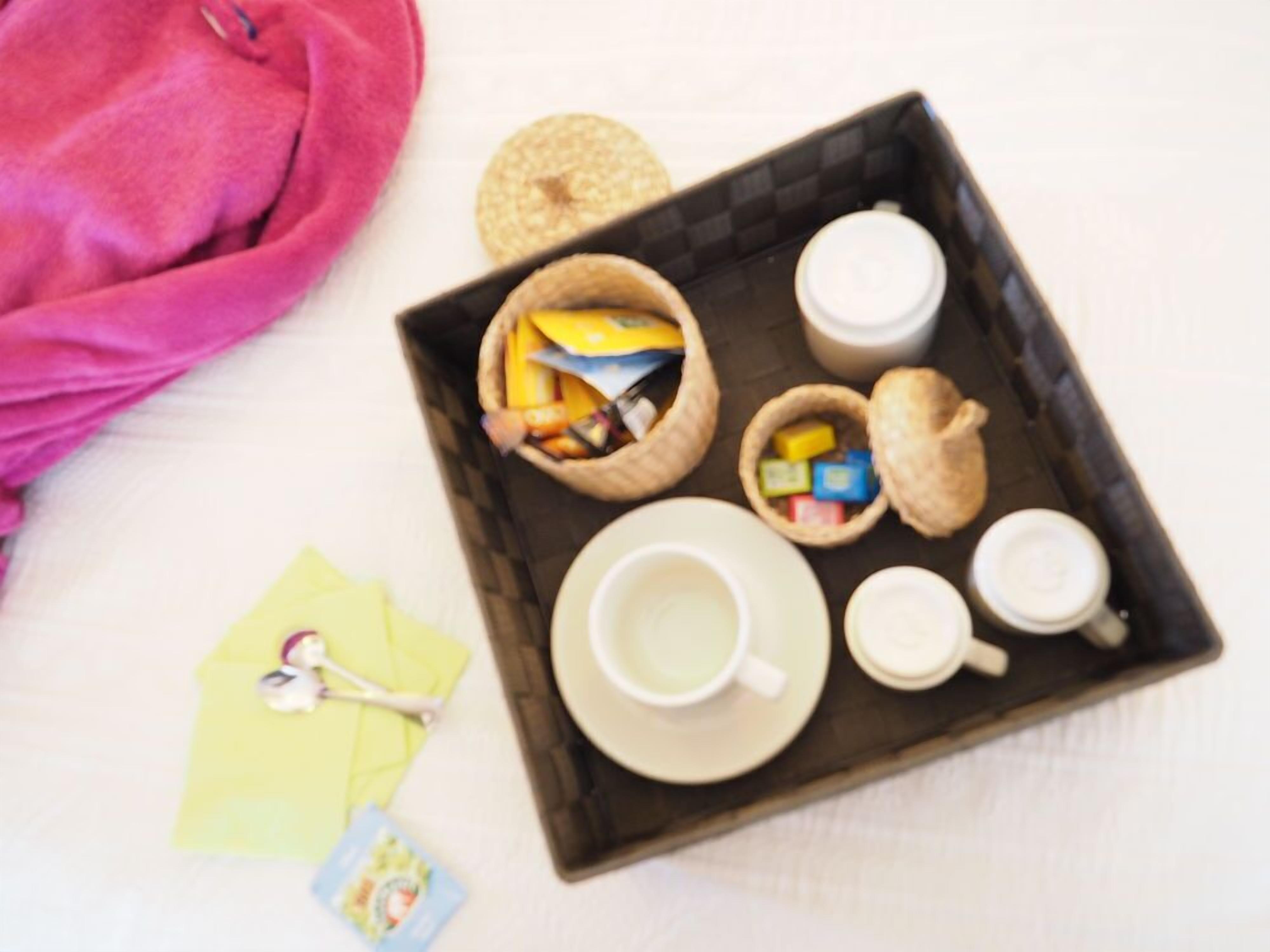 A tray with a cup, two mugs, and a basket containing snacks and a biscuit.