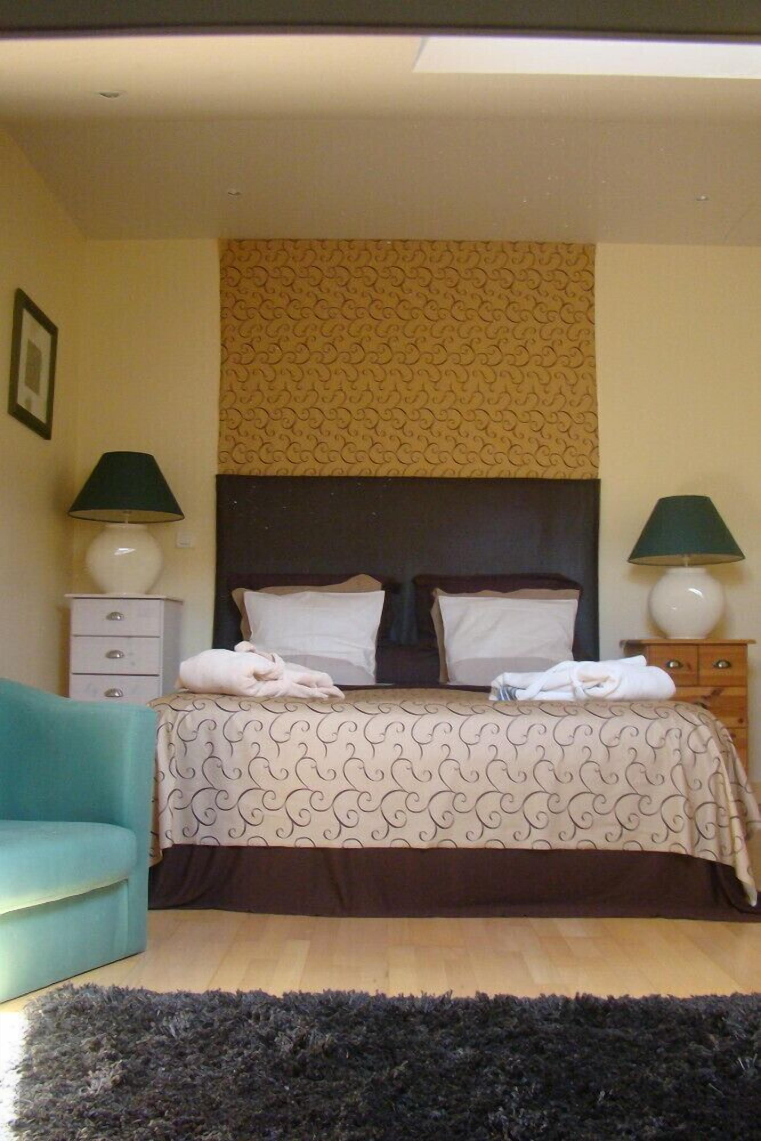 A hotel room with a bed, two bedside tables with lamps, a chair, and a patterned headboard.