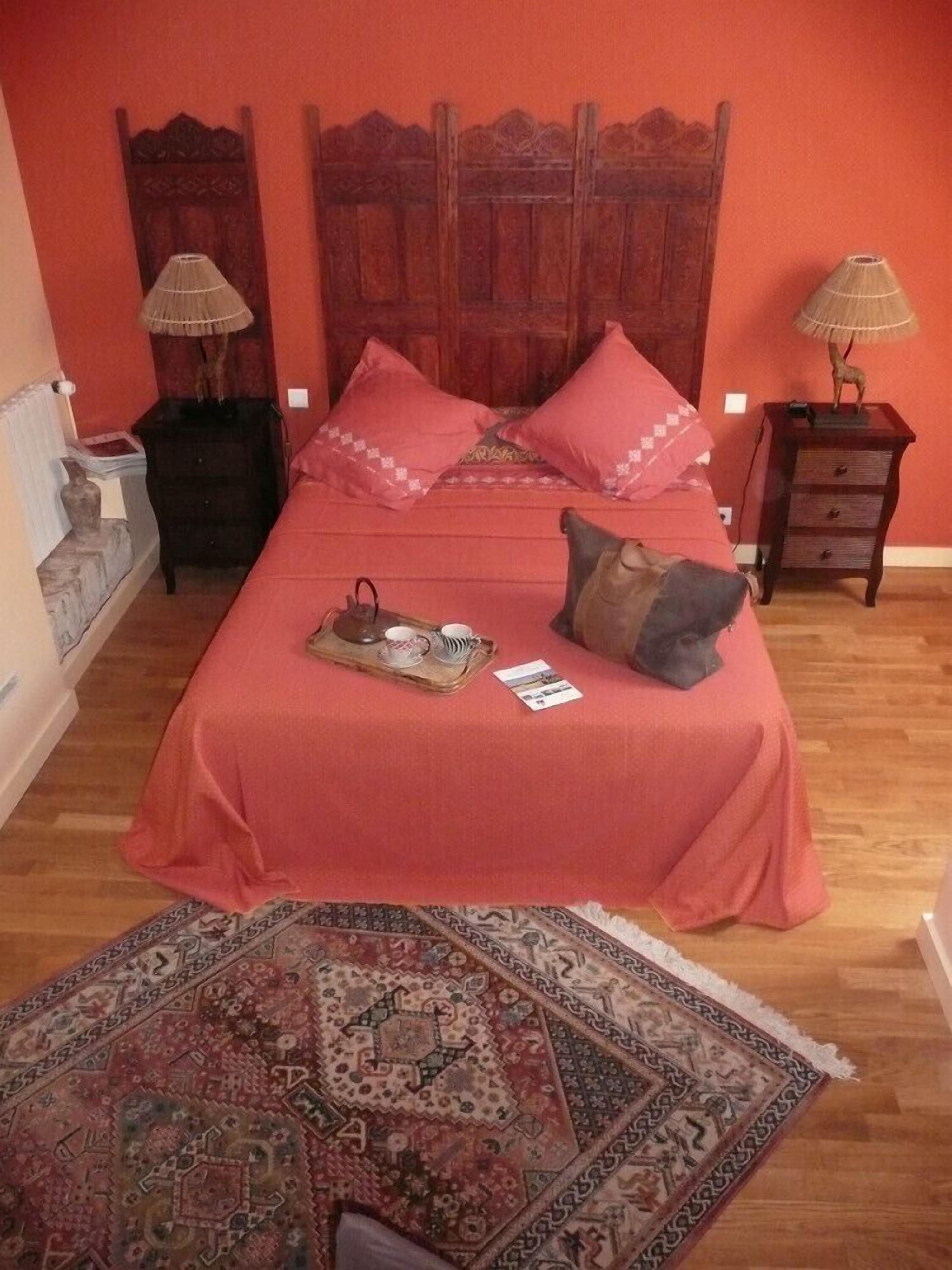 A room with a wooden bed, two nightstands, a patterned rug, and a red wall.