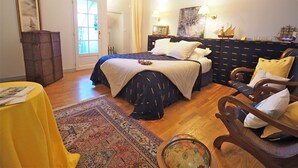 A bedroom with a large bed, a wooden chest, a small table with magazines, a patterned rug, and a globe. - Chambres d'hôtes La Bruyère (May-sur-Orne)