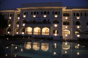 A hotel with a pool, multiple balconies, and warm lighting.