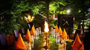 Une table dressée pour le dîner, avec des serviettes orange, des verres transparents et un chandelier allumé en guise de centre de table.