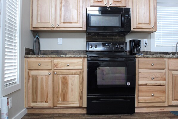 A kitchen with wooden cabinets, a black microwave, a stove, and a coffee maker.