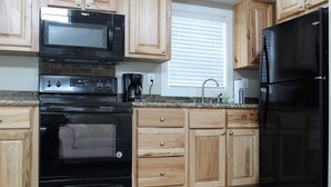 A kitchen with wooden cabinets, a black refrigerator, a black microwave, and a black oven.