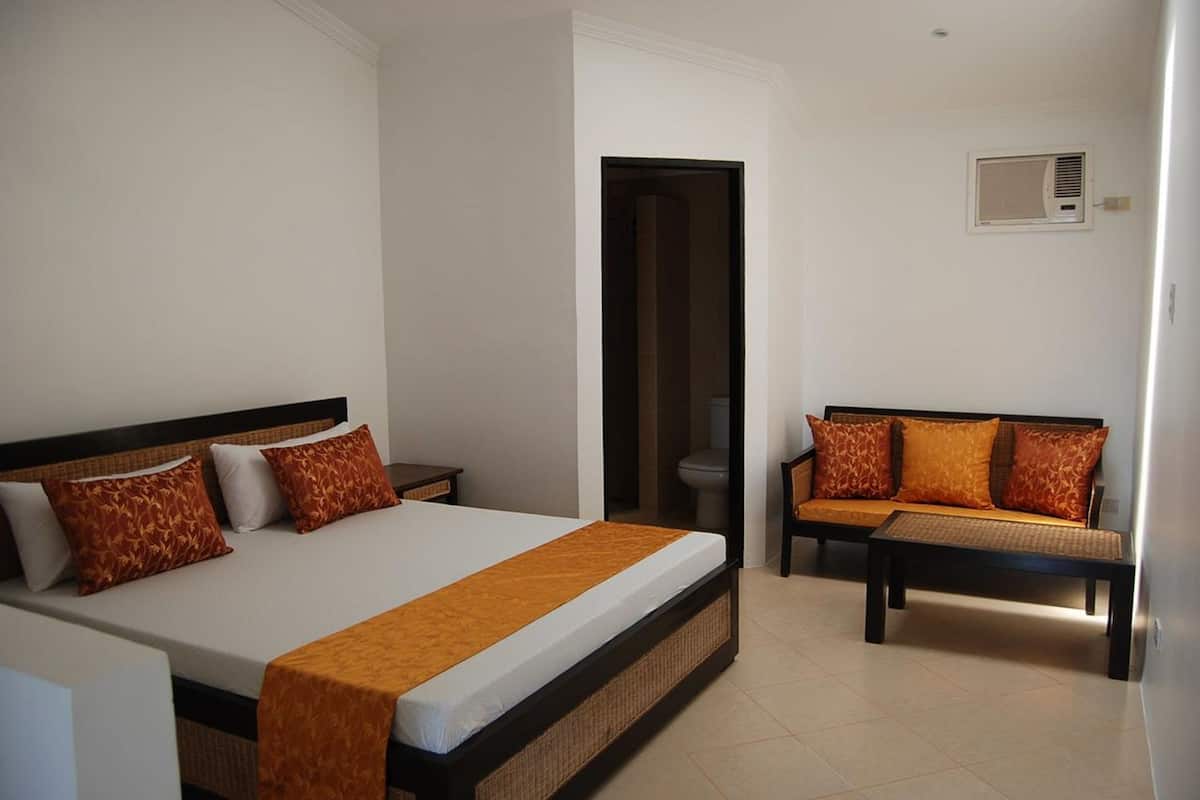 Une chambre d’hôtel équipée d’un lit, d’un canapé, d’une petite table et d’un climatiseur fixé au mur.