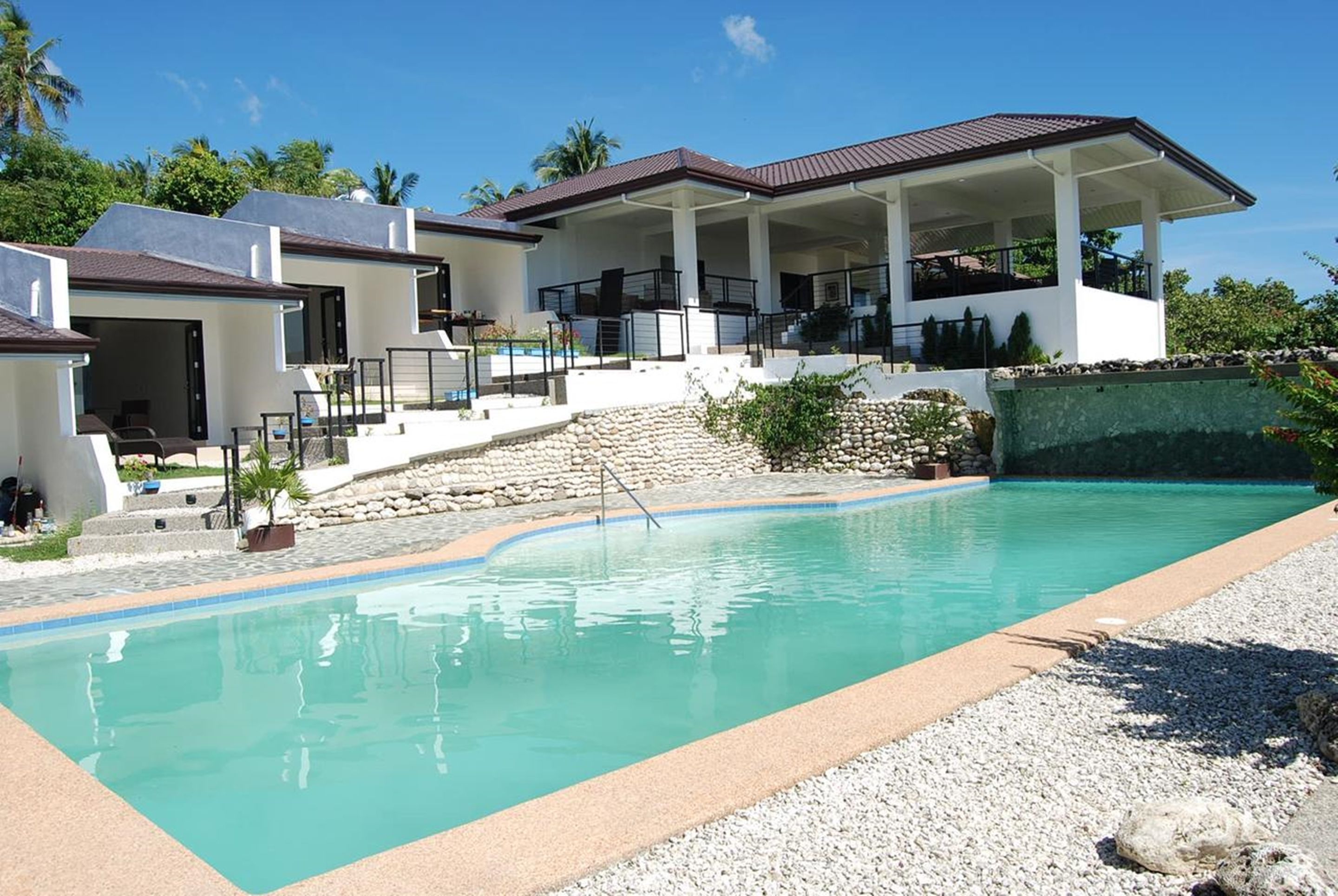 A modern resort with a large swimming pool, multiple guest villas, and a covered outdoor area.