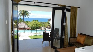 A room with a sliding glass door leading to a balcony with a pool and ocean view.