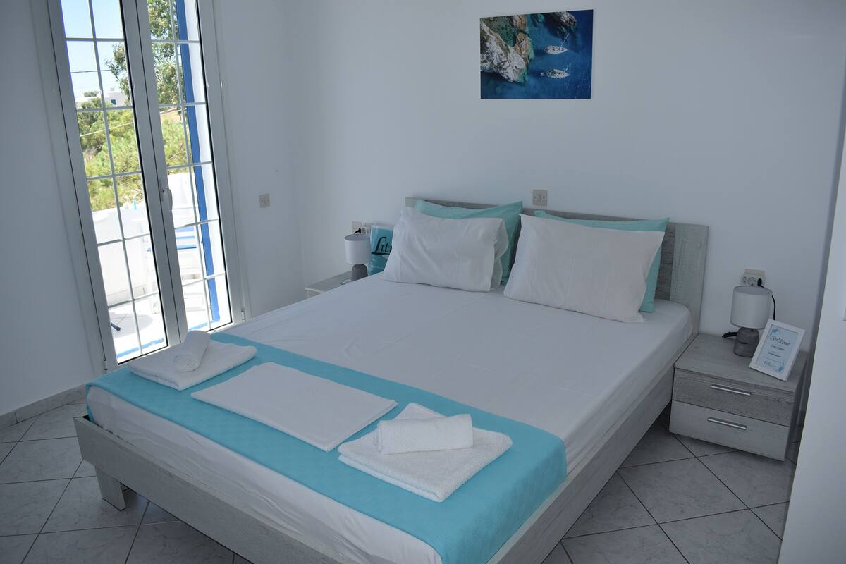Un lit bien fait, avec une literie blanche et turquoise, une table de chevet avec une lampe et un tableau accroché au mur.