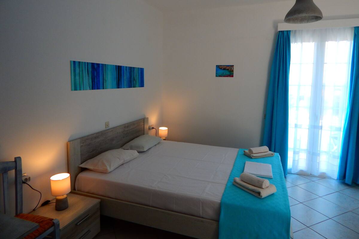 Une chambre à coucher avec un lit, des lampes de chevet, un rideau bleu et un petit tableau accroché au mur.