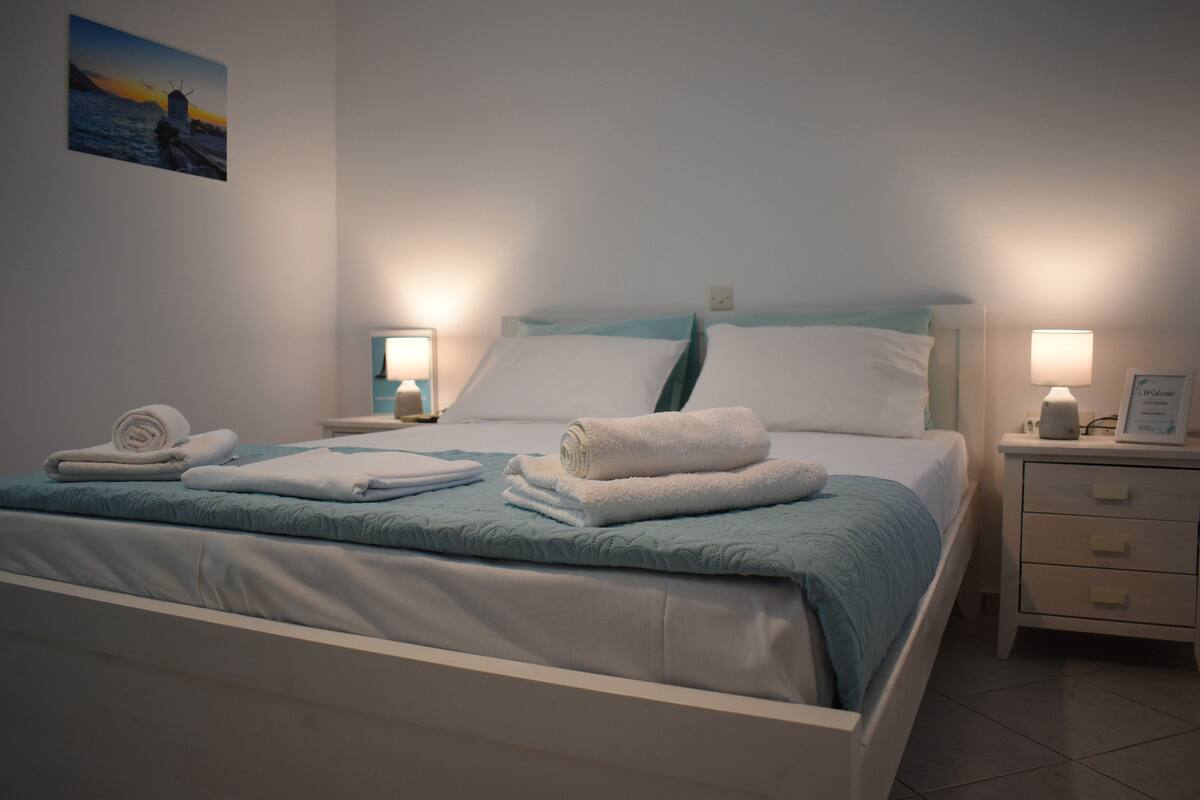 Un lit bien fait, avec une literie blanche et bleue, deux tables de chevet avec des lampes et un tableau accroché au mur.