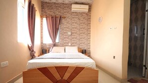 A bedroom with a bed, curtains, a brick-patterned wall, an air conditioner, and a wooden headboard. - Parigha Hotel (Accra)