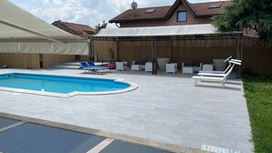 Patio trasero con piscina, sillas de descanso y un área de estar techada.