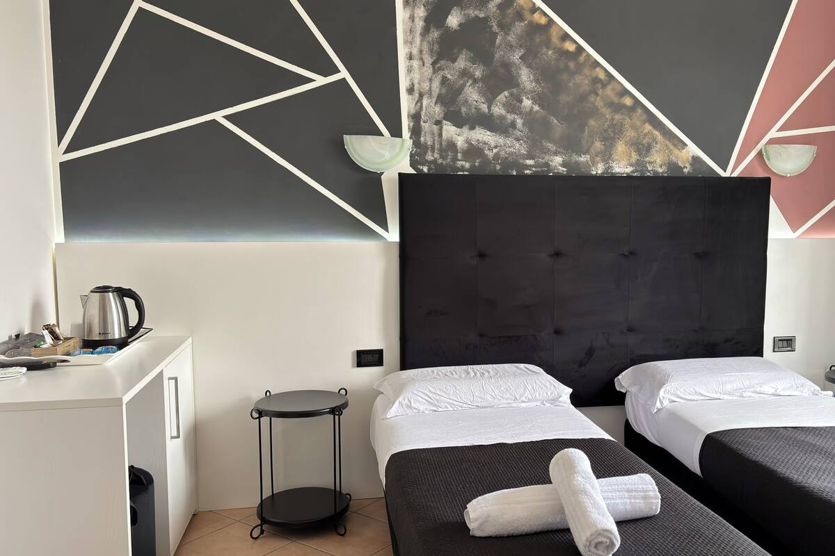 Habitación de hotel con dos camas, un escritorio, un hervidor de agua y una pared con diseños geométricos.
