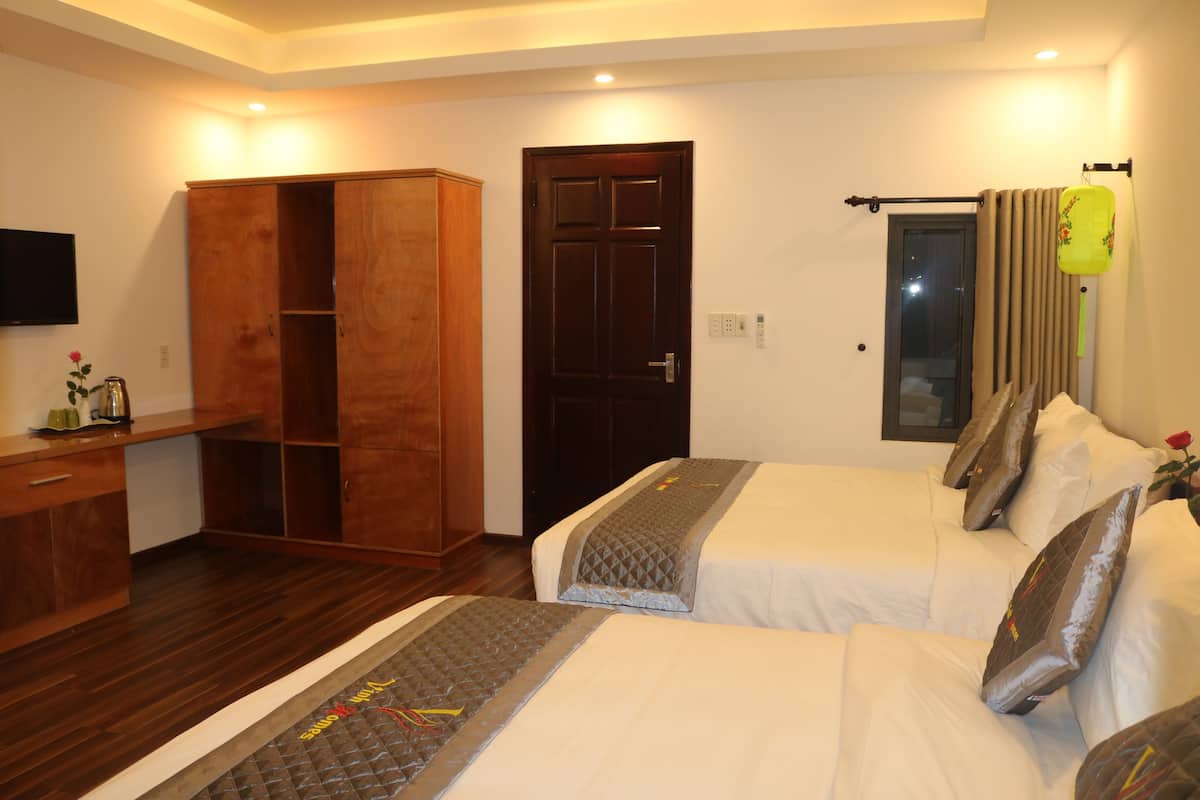 A hotel room with two beds, a wooden wardrobe, a desk, and a television on the wall.