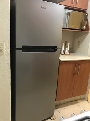 Compact kitchen with a refrigerator, cabinet, and microwave.