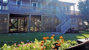 Ein zweistöckiges Holzhaus mit überdachter Terrasse und einer Treppe, die zum Obergeschoss führt.