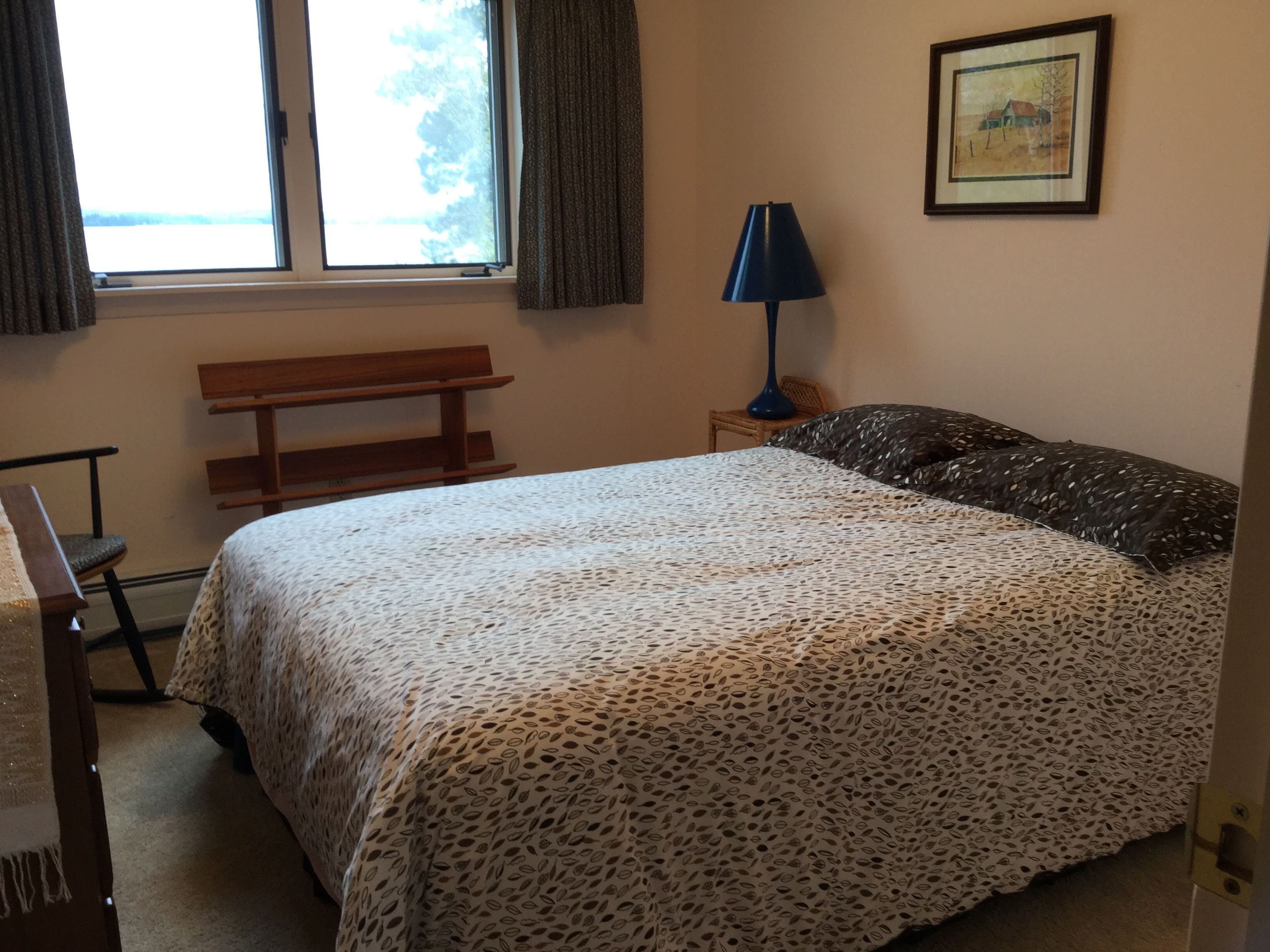 A bedroom with a bed, a bench, a desk, a lamp, and a framed picture on the wall.