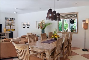 Enjoy meals in this dining area with a rustic table and six chairs, surrounded by a modern ceiling fan and a large window with a view of the outdoors.