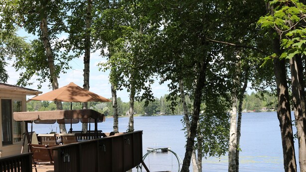 Une terrasse en bois avec des meubles d’extérieur, un fauteuil suspendu et une vue sur un lac.
