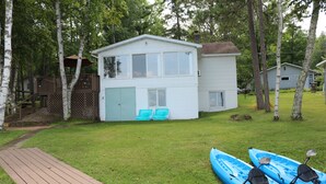 Une maison à deux étages avec une terrasse, un petit abri de jardin et des kayaks dans la cour.