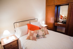 A neatly made bed with white and orange pillows, a bedside lamp, and a wooden nightstand. - Traditional Luxury Villa Armonia (Aigialeia)