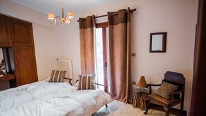 A bedroom with a large bed, a chair with a leopard print pillow, a wooden side table, and a mirror on the wall. - Traditional Luxury Villa Armonia (Aigialeia)