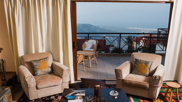 A balcony with two beige armchairs, a wooden coffee table, and a view of the sea and mountains. - Traditional Luxury Villa Armonia (Aigialeia)
