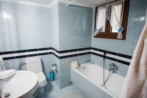 A bathroom with a toilet, sink, and bathtub, tiled in light blue and white, with a window and curtains. - Traditional Luxury Villa Armonia (Aigialeia)