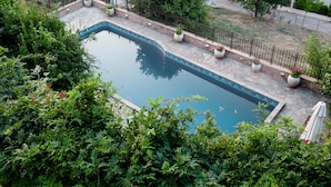 A rectangular swimming pool with a stone border, surrounded by lush greenery and potted plants. - Traditional Luxury Villa Armonia (Aigialeia)