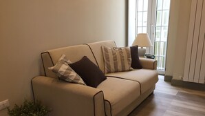 A beige sofa with two pillows, a small table with a lamp, and a potted plant. - Dimora Spina in Centro (Campobasso)