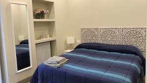 A bedroom with a bed, a bedside table, a mirror, a shelf with toiletries, and decorative wall paneling. - Dimora Spina in Centro (Campobasso)