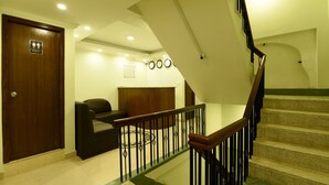 A staircase with a wooden handrail and black balusters, leading to a landing with a dark leather sofa and a wooden headboard. - Hotel Ruza Nepal (Kathmandu)