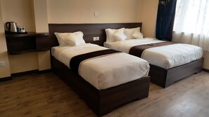 A hotel room with two single beds, a wooden floor, a nightstand with a kettle and glasses, and a window with curtains. - Hotel Ruza Nepal (Kathmandu)