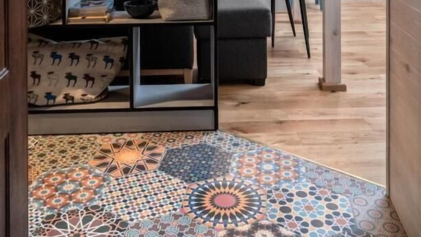 Ein modernes Wohnzimmer mit Holzboden, einem gemusterten Teppich, einer schwarzen Couch und einem Bücherregal voller Bücher und Dekoartikeln.