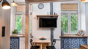 Eine moderne Küche mit an der Wand montiertem Fernseher, Holzschränken und einem Fenster mit Jalousien.