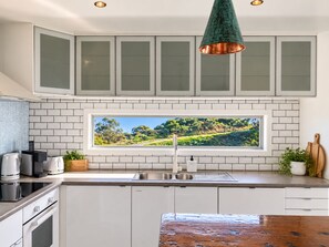 Cozinha moderna com armários brancos, ilha planejada, pia de aço inoxidável e uma grande janela com vista panorâmica.