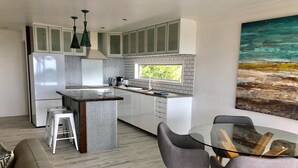 Une cuisine moderne avec des meubles blancs, un îlot central et un coin repas comprenant une table en verre et des chaises grises.