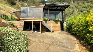 Une maison moderne dotée d’une terrasse en bois, d’un espace extérieur couvert et offrant une vue sur les collines environnantes.