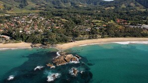 Vue aérienne d’une ville côtière avec une plage, une côte rocheuse et des collines environnantes.