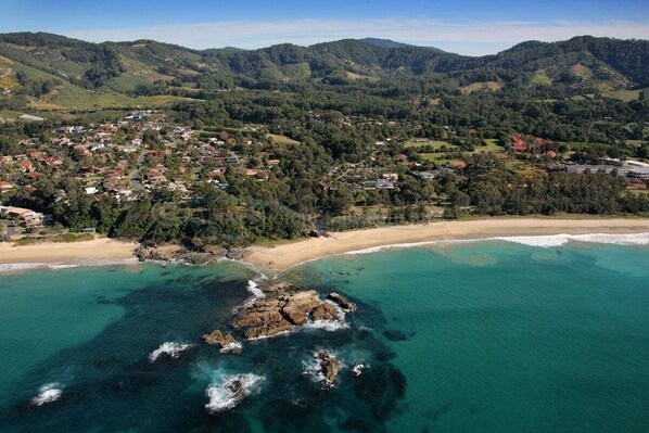 An aerial view of a coastal town with a beach, rocky coastline, and surrounding hills. - Sky Loft Coffs · Sky Loft On Bruxner - Korora (Korora)