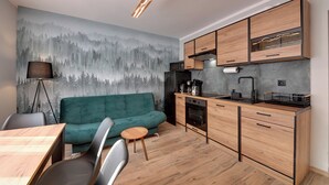 A modern kitchen with wooden cabinets, a built-in microwave, and a dining area with a green sofa and a small round table. - RentPlanet - Apartament Bronka Czecha (Swieradow-Zdroj)