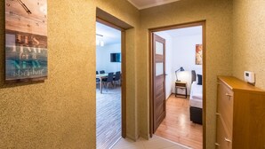 A hallway with a wooden floor, a clock, and a door leading to a bedroom with a bed and a nightstand. - RentPlanet - Apartament Bronka Czecha (Swieradow-Zdroj)