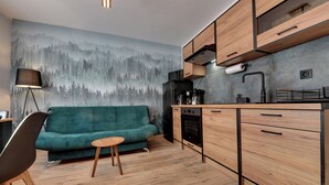 A modern kitchen with wooden cabinets, a green sofa, and a forest mural on the wall. - RentPlanet - Apartament Bronka Czecha (Swieradow-Zdroj)