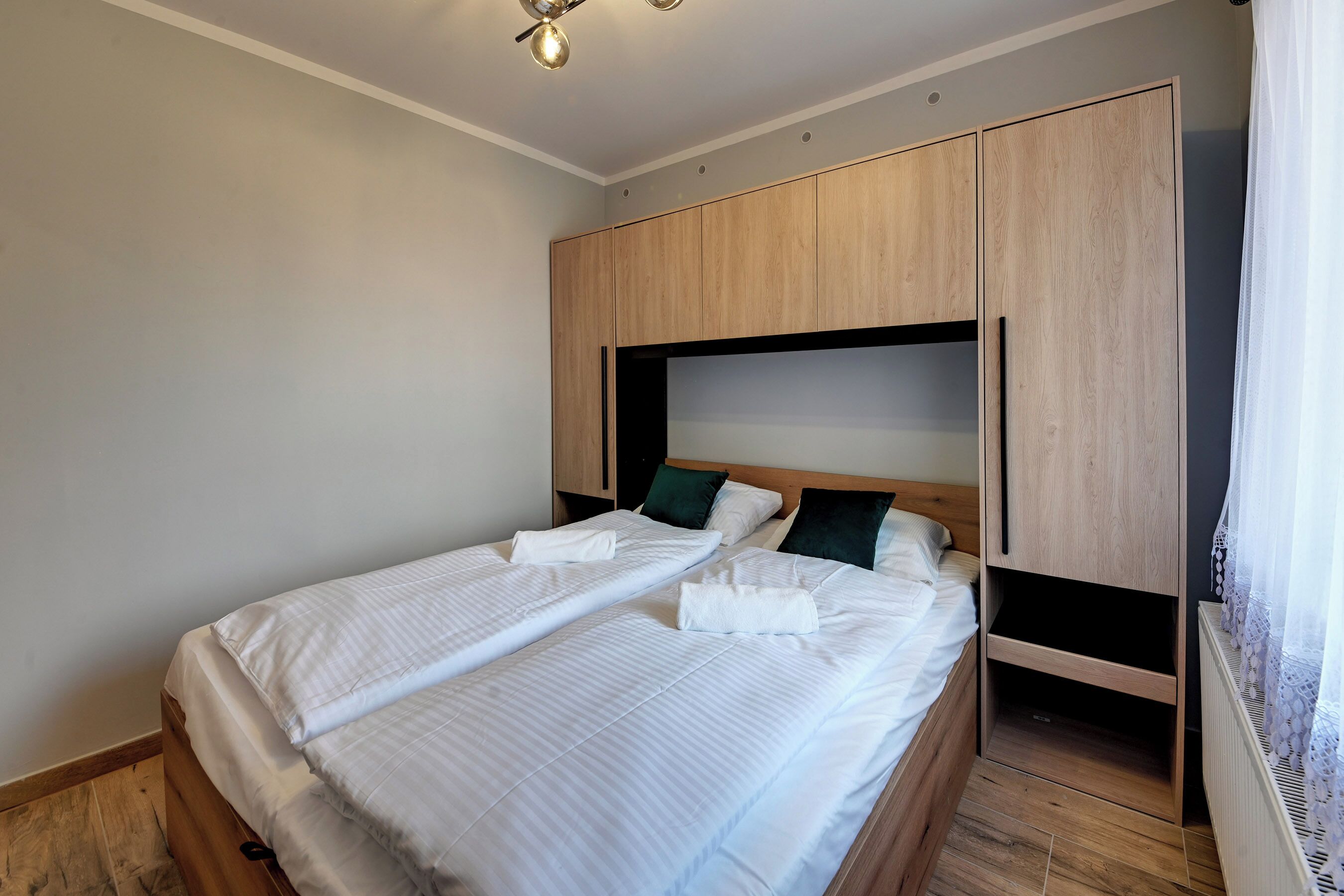 A bedroom with two beds, wooden wardrobe, and a ceiling light.