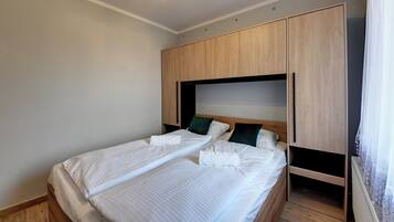 A bedroom with two beds, wooden wardrobe, and a ceiling light.