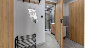 A hallway with a black metal rack, a wooden door, and a shower area with a patterned wall. - RentPlanet - Apartament Bronka Czecha (Swieradow-Zdroj)